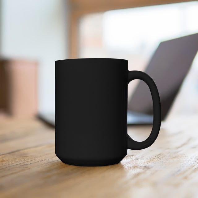 Back view of a matte black 15oz Sumato Coffee Co. mug on a wooden desk with a blurred laptop in the background — clean and bold workspace vibes.