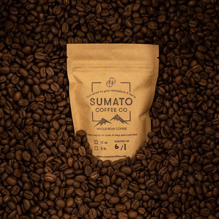 Sumato Coffee Co. whole bean bag nestled in a bed of roasted coffee beans, kraft paper packaging with roast date and weight options shown