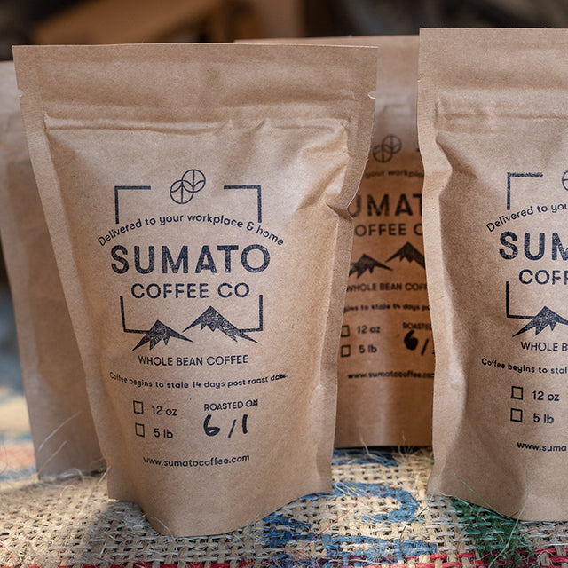Close-up of Sumato Coffee Co. whole bean sample bags labeled with roast date, displayed on burlap with kraft paper packaging