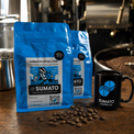 Blue Sumato Coffee bags and branded mug beside freshly roasted coffee beans at the roastery